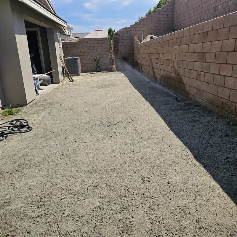 A picture of the side of a house which has been leveled so that the dirt and sand is ready for planting.